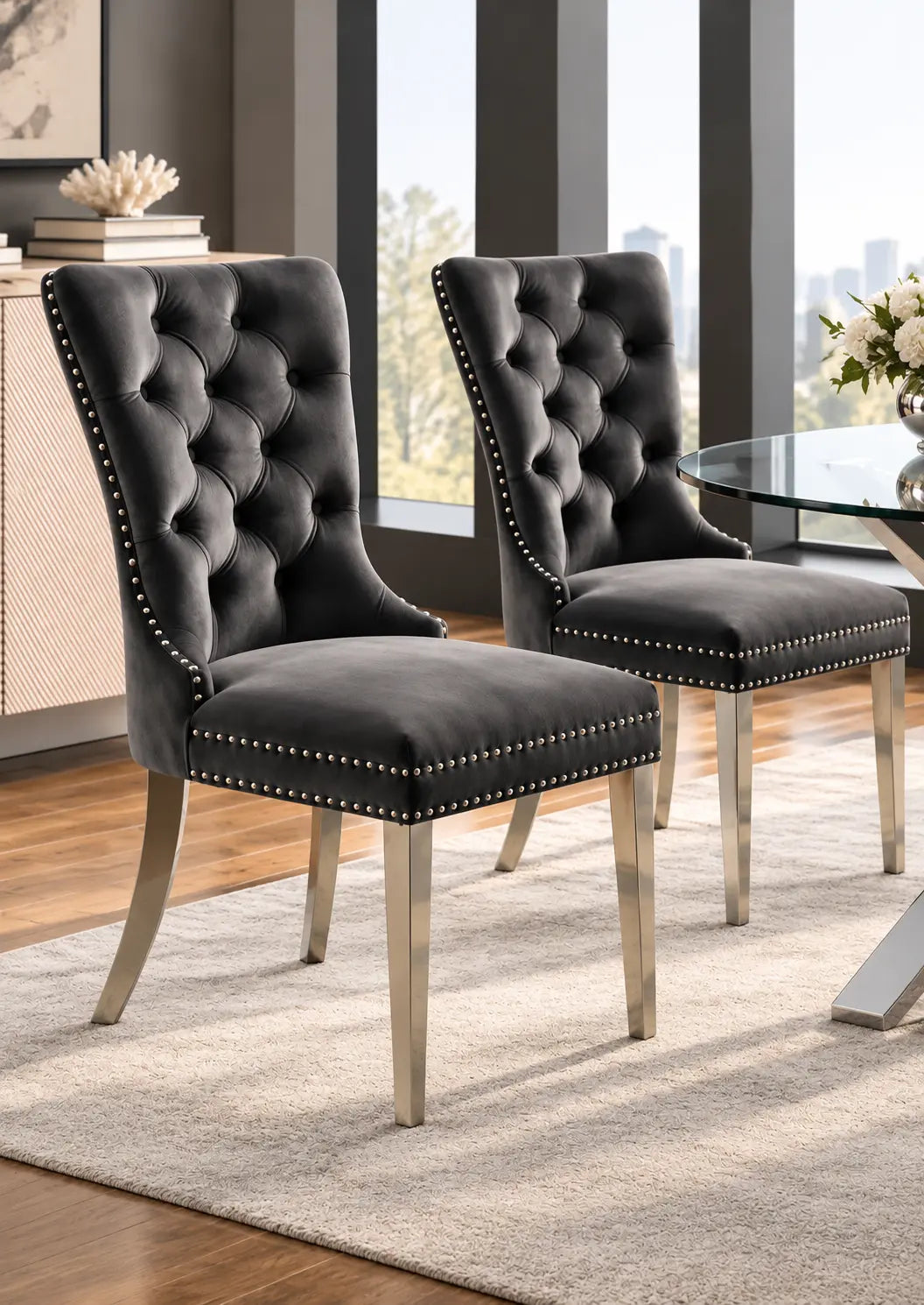 Deux chaises en velours gris, avec un design élégant et un cadre en chrome poli, sont placées autour dune table.