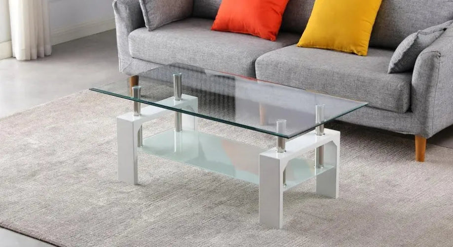 Table basse Optimum Plus en verre avec pieds en chrome, moderne et élégante, placée devant un canapé gris avec coussins.