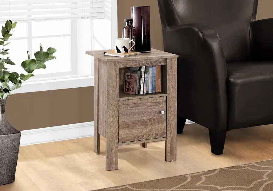 Table daccent Optimum Plus en taupe foncé, en bois, avec un tiroir et une étagère, placée près dun fauteuil.